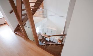 A shot of the wooden stairs showing different levels from the top featuring curved detail and glass barriers.