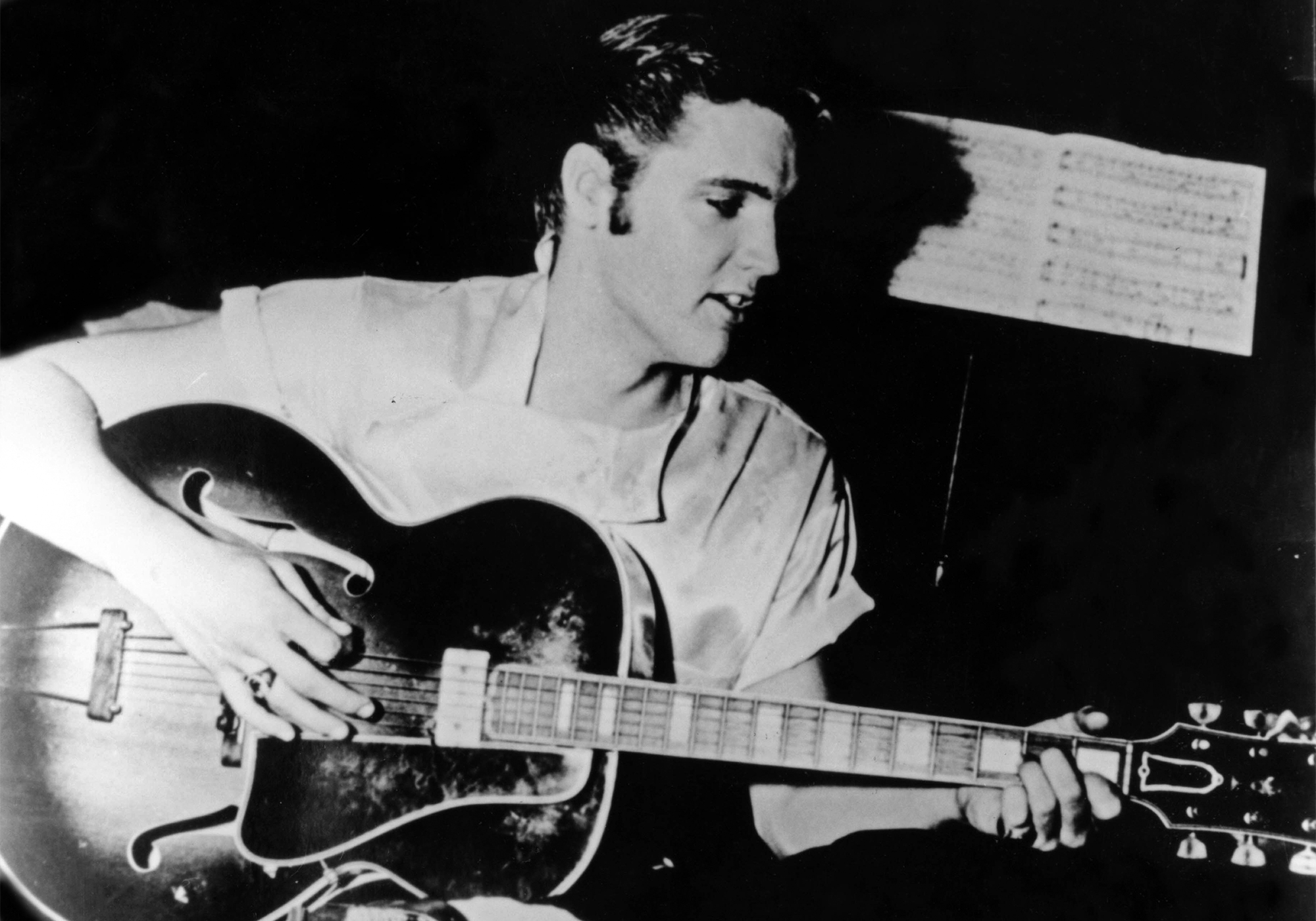 UNITED STATES - JANUARY 01: USA Photo of Elvis PRESLEY, Playing guitar. Sitting on stool. With sheet music behind, c.1956