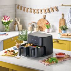 Aldi dual basket air fryer on kitchen worktop surrounded by cooked dishes