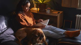 Woman sitting on sofa reading a book about relationship burnout with sleeping dog next to her