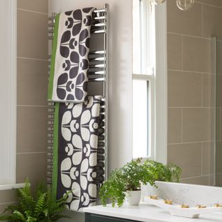 Patterned towels hung on a heated towel rail above a bath in a tiled bathroom