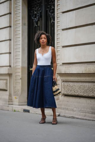 PARIS, FRANCE - MAY 08: Ellie Delphine wears golden earrings, a necklace, a white tank top, a blue midi denim gathered skirt, a beige and black striped fluffy bag, black leather sandals with straps, during a street style fashion photo session, on May 08, 2024 in Paris, France. (Photo by Edward Berthelot/Getty Images)
