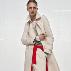 Woman wears cream trench coat, green knit, cream trousers
