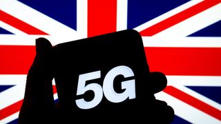 A shadow of hand holding a smartphone with "5G" displayed on screen. UK flag is seen in the background.