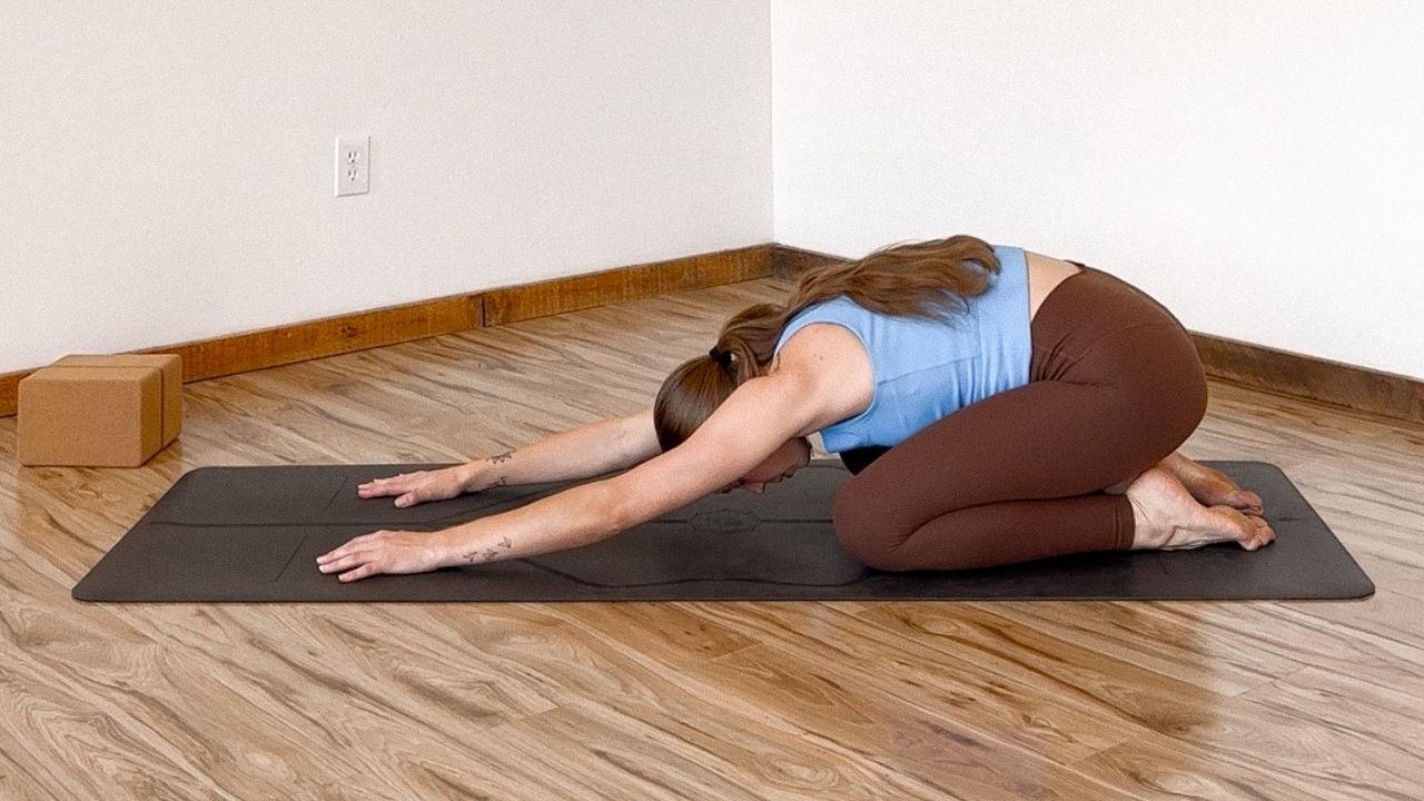 Woman in brown leggings and blue tank top demonstrates yoga pose