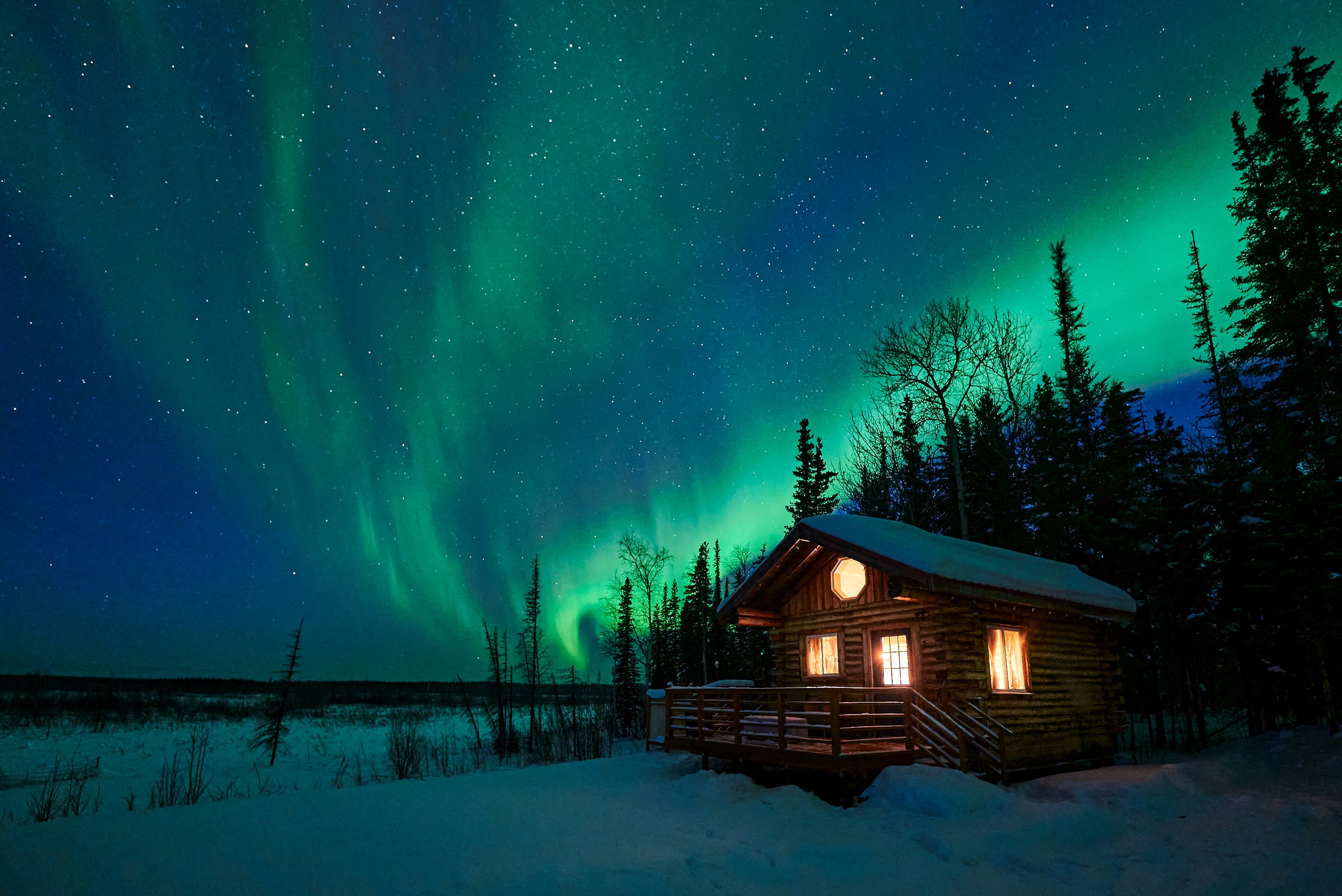 A peaceful scene of a cabin in a snowy Alaskan landscape with the northern lights overhead.