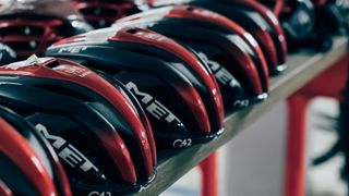 A line of MET Trenta helmets in UAE Team's black and red Colours sit on a table in the UAE Team's service course
