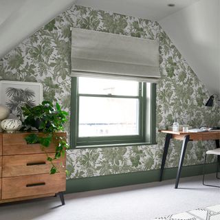 A loft space converted into a home office with green floral wallpaper and green painted windows