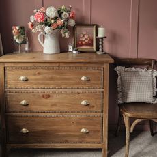 A vintage-style IKEA HEMNES dresser with a bobbin trim and scalloped handles and a jug filled with flowers on top set against a pink panelled wall