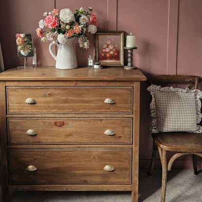 A vintage-style IKEA HEMNES dresser with a bobbin trim and scalloped handles and a jug filled with flowers on top set against a pink panelled wall