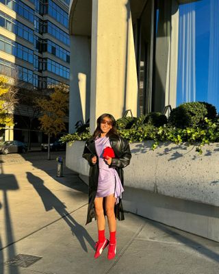 Michelle wears a purple dress with red Puma Speedcats, a red handbag, and a long black coat.