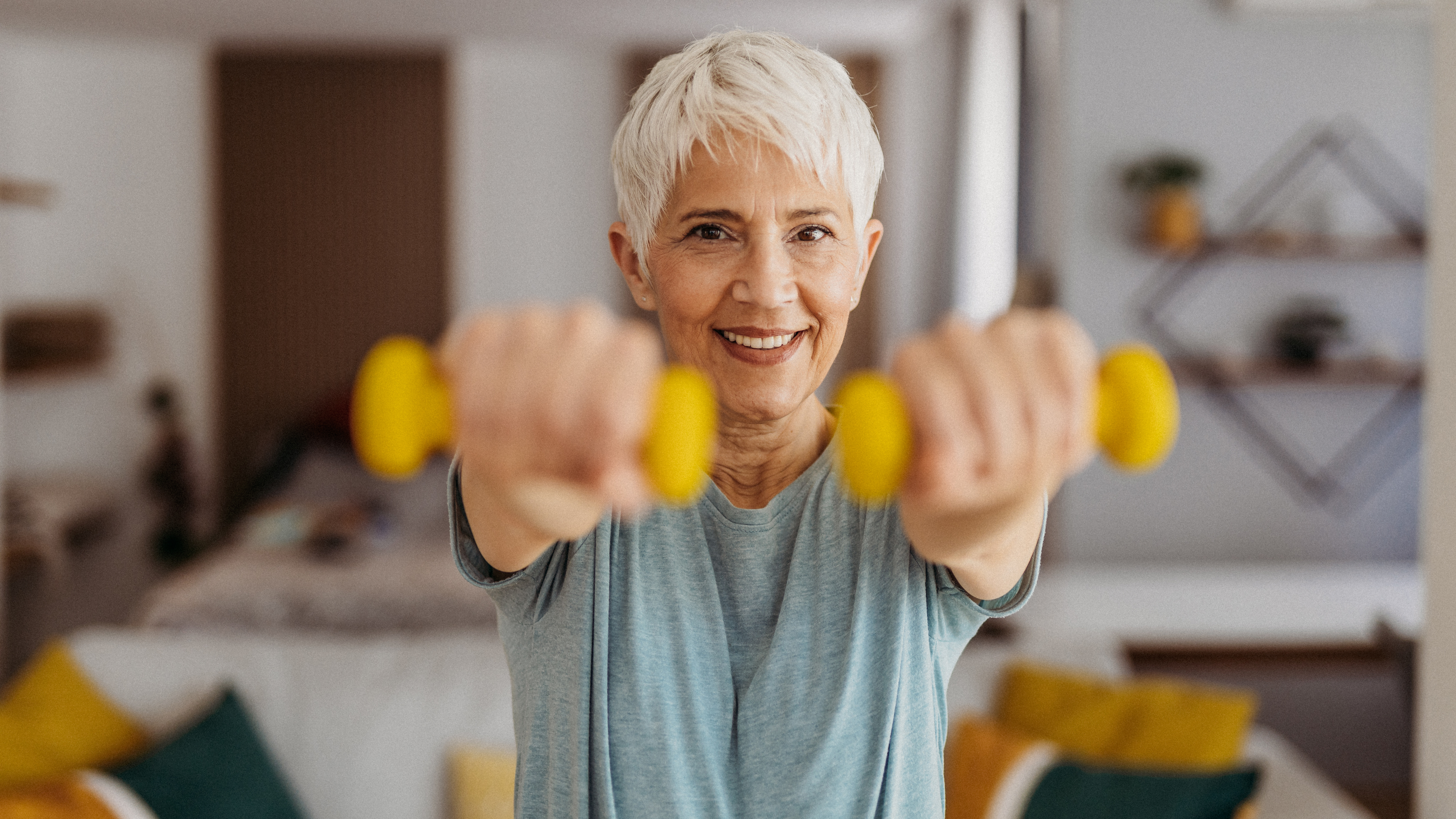 A woman holds dumbbells in her hands, arms extended in line with her shoulders.