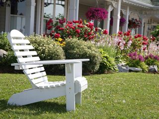 A white chair in front of a house and flower garden