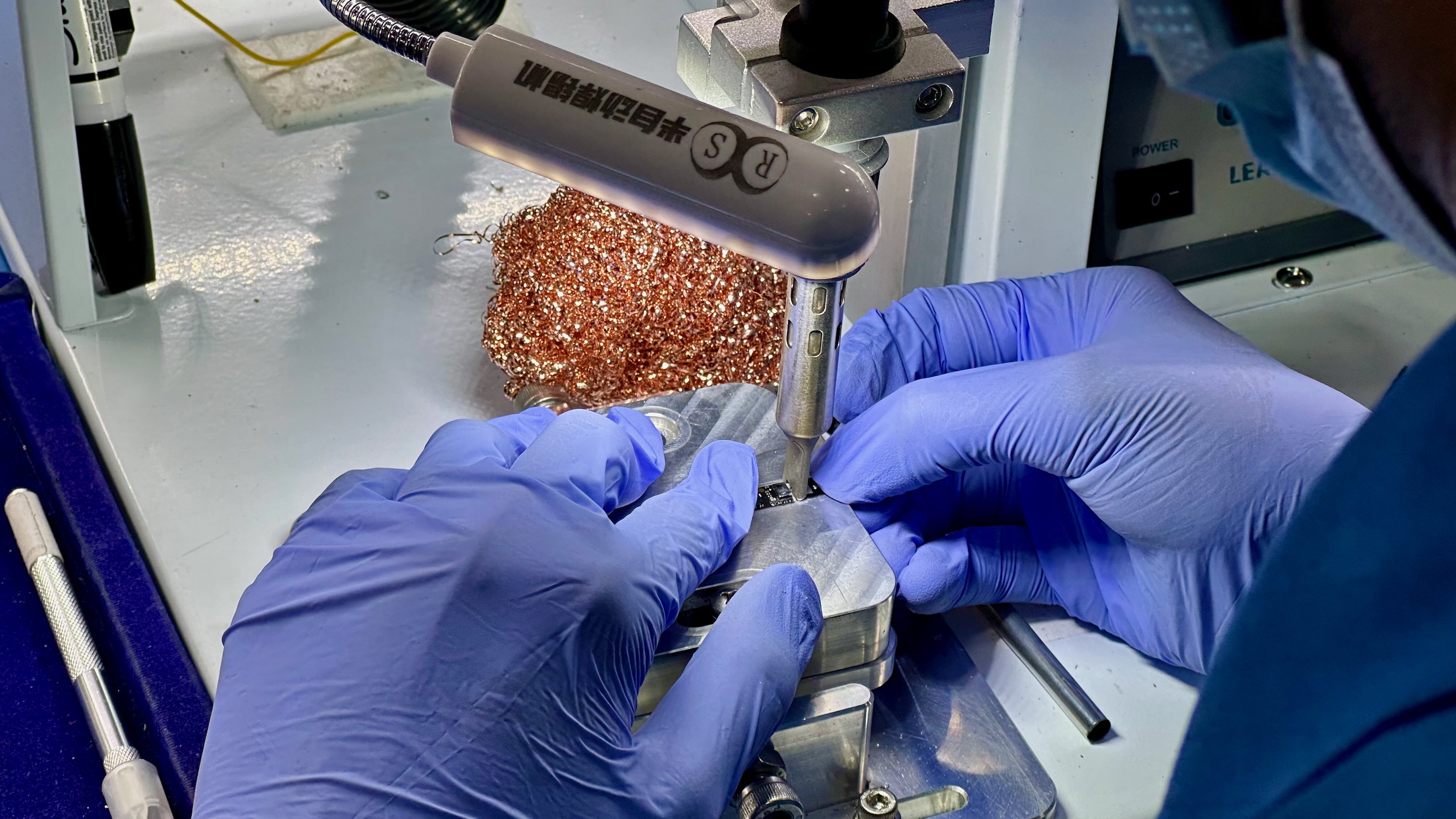 An Ultrahuman factory worker using a machine to solder two Ring Air components together.