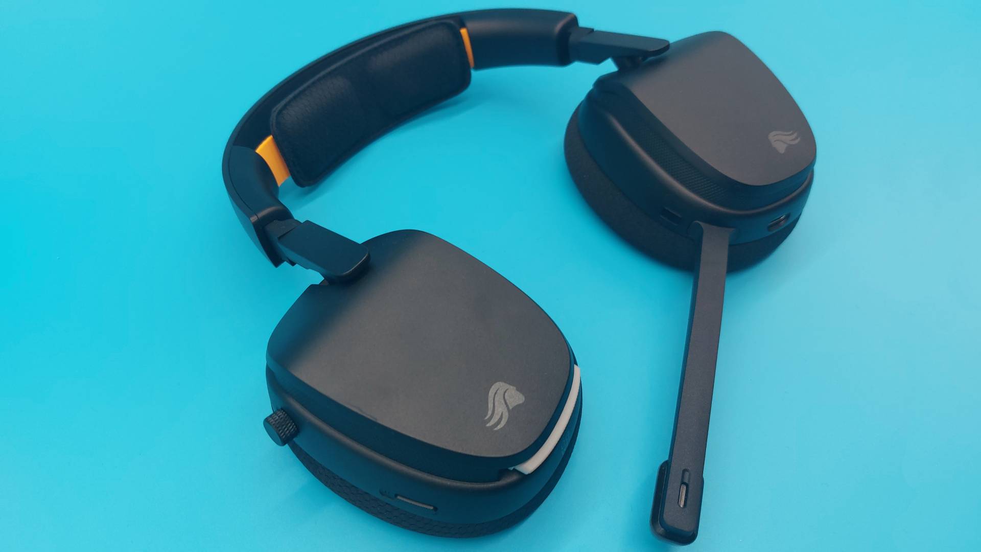 The GHS Wireless InfinitePlay seen from various angles on a blue background. This is a wireless gaming headset from Glorious. It is black all over, save for a few subtle orange accents.