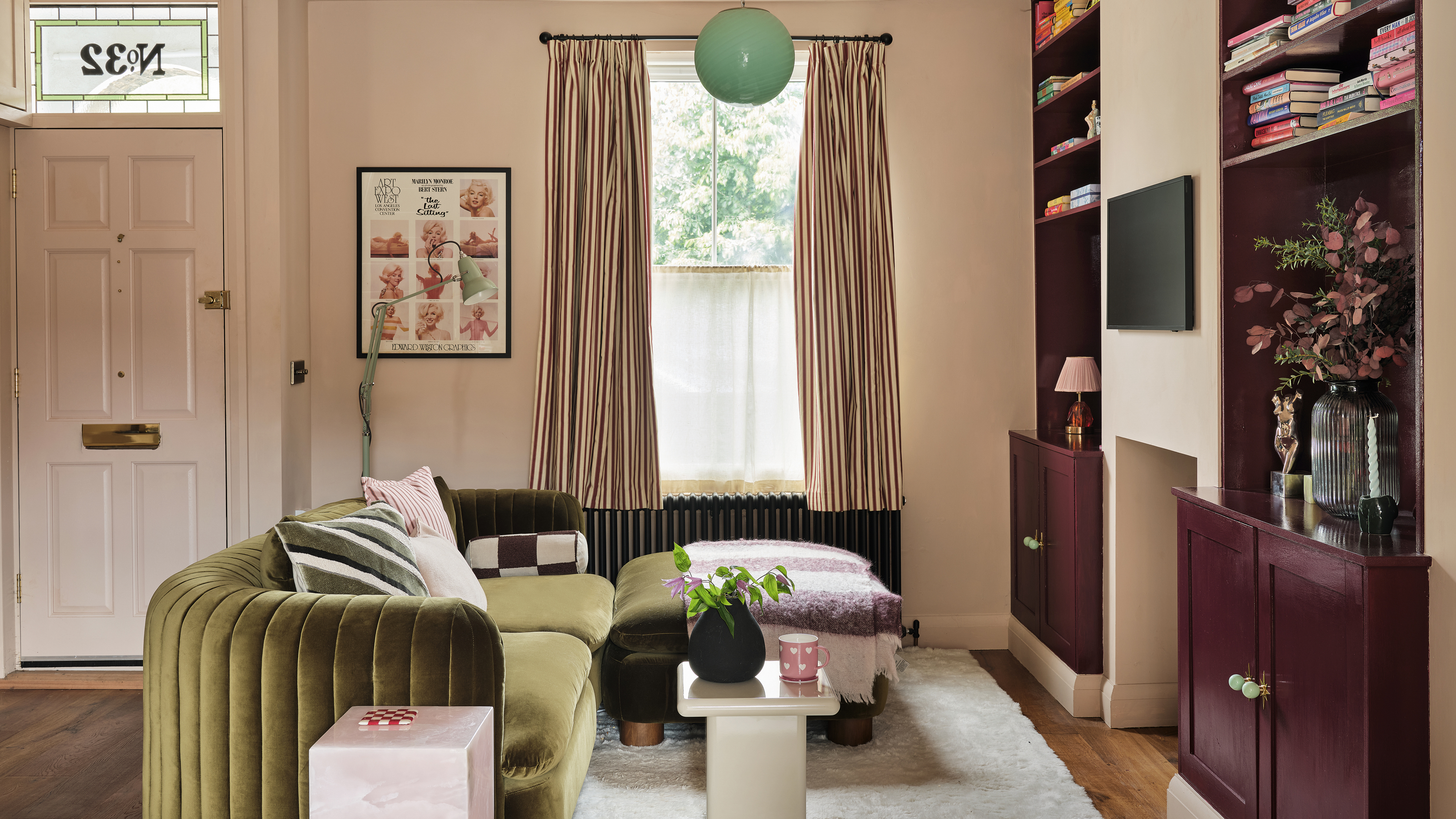 a small living room with a green velvet sofa and dark burgundy fitted alcove shelving and cabinetry and a front door