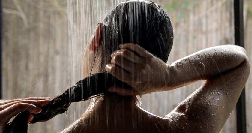 a photo of a woman in warm shower washing hair as part of nighttime routine 