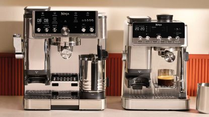 Image of a silver Ninja Luxe Cafe Pro machine next to a silver Ninja Luxe Cafe Mini machine on a countertop with an orange backsplash.