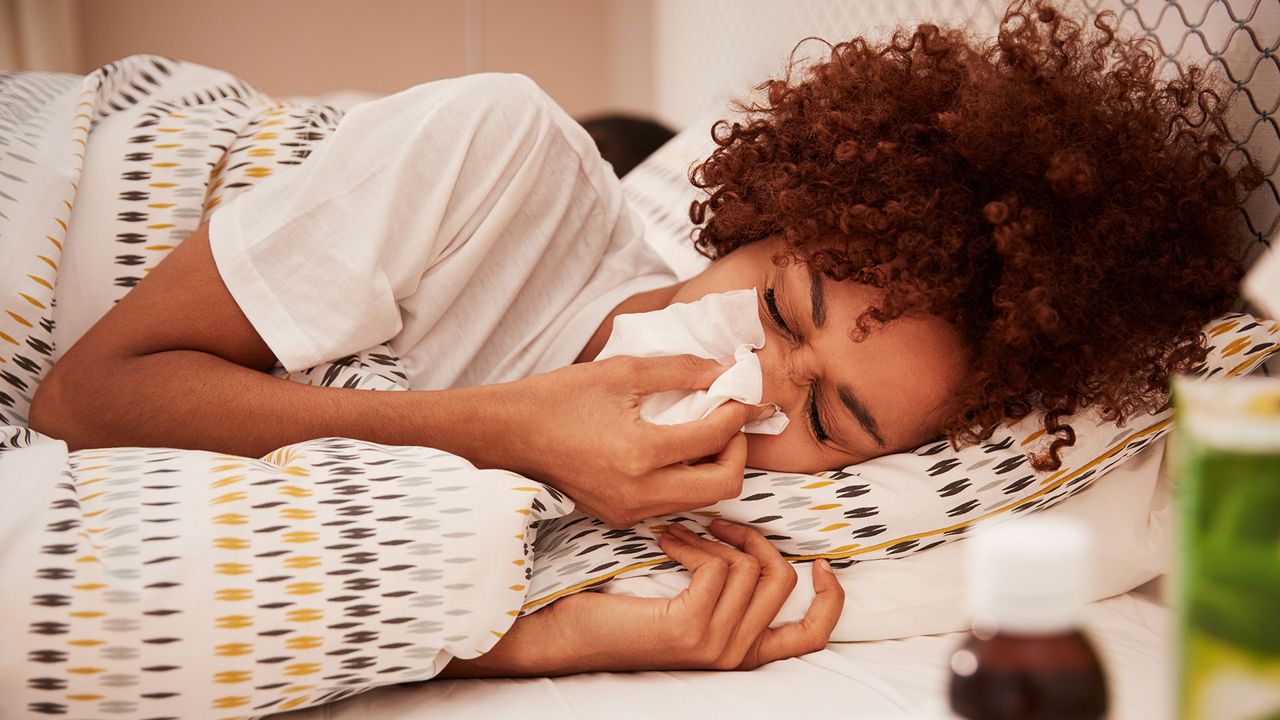 Woman lying in bed, blowing her nose