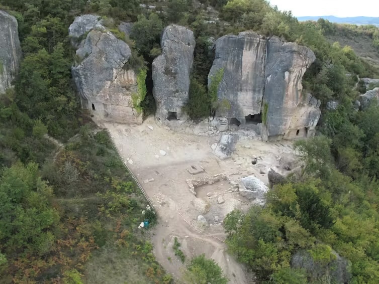 An aerial view of cave entrances at the bottom of a tall cliff in the forest