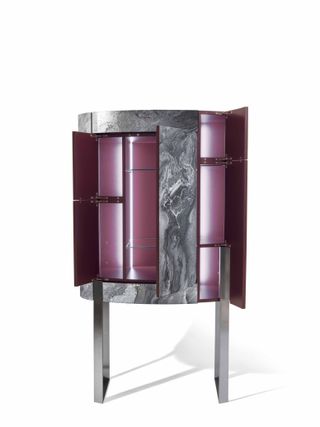 A tall drinks cabinet with open doors. The outside is clad in metal sheet with marbled effect, while the inside is made of wood painted burgundy colour