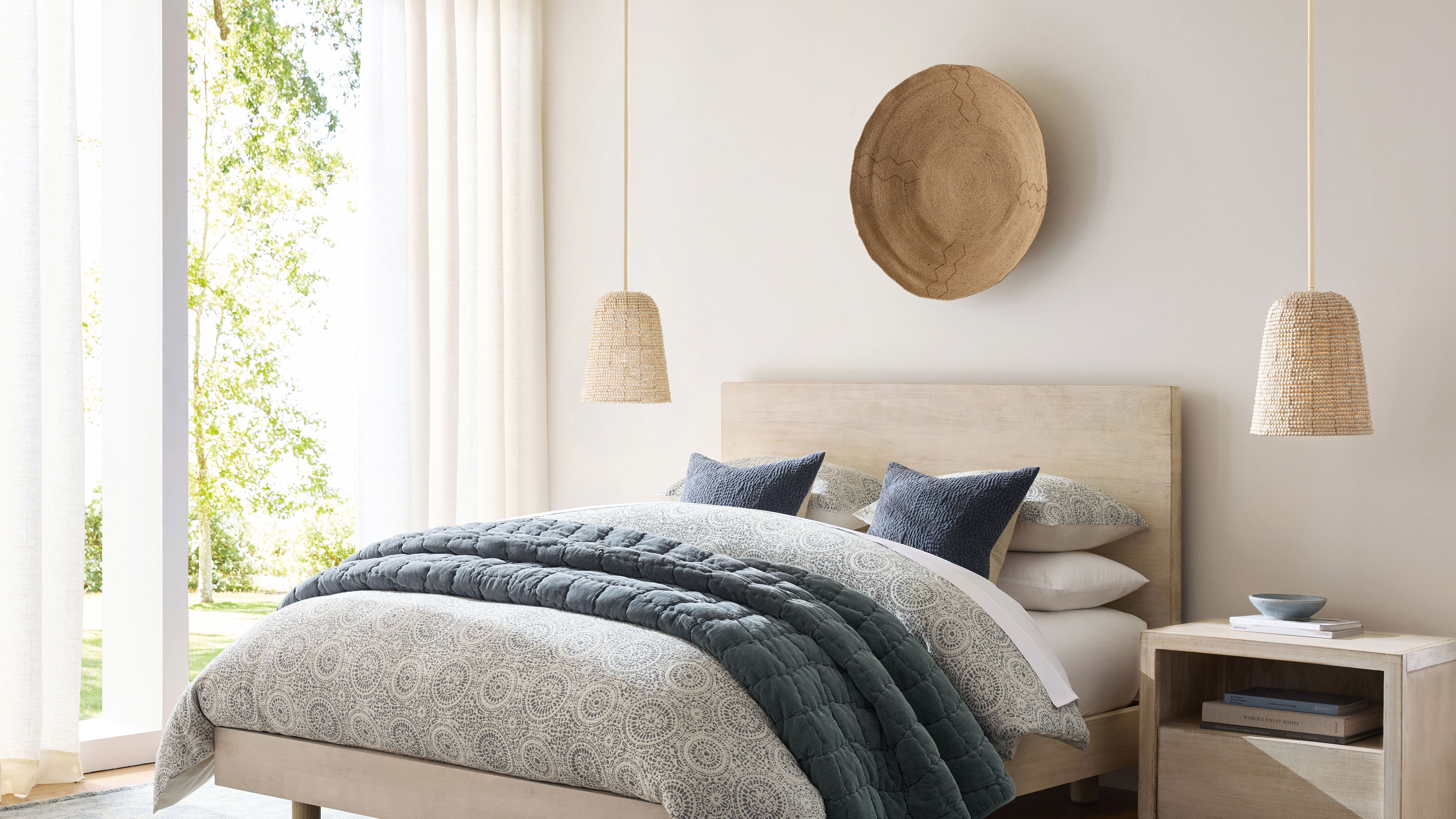White bedroom with two pendant bedside lamps, a rattan bowl hung above the headboard