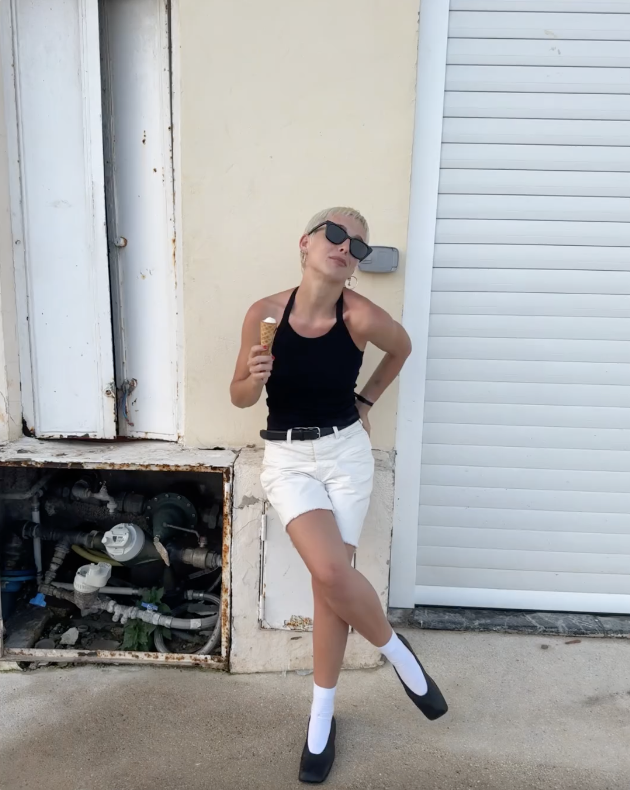 @emmachamberlain wears white denim shorts with a black tank top and black square-toe ballet flats.