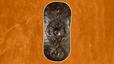 a tall bronze shield with red roundel decorations against an orange background