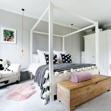 bedroom with grey wall white frame bed with designed cushion and wooden table seat