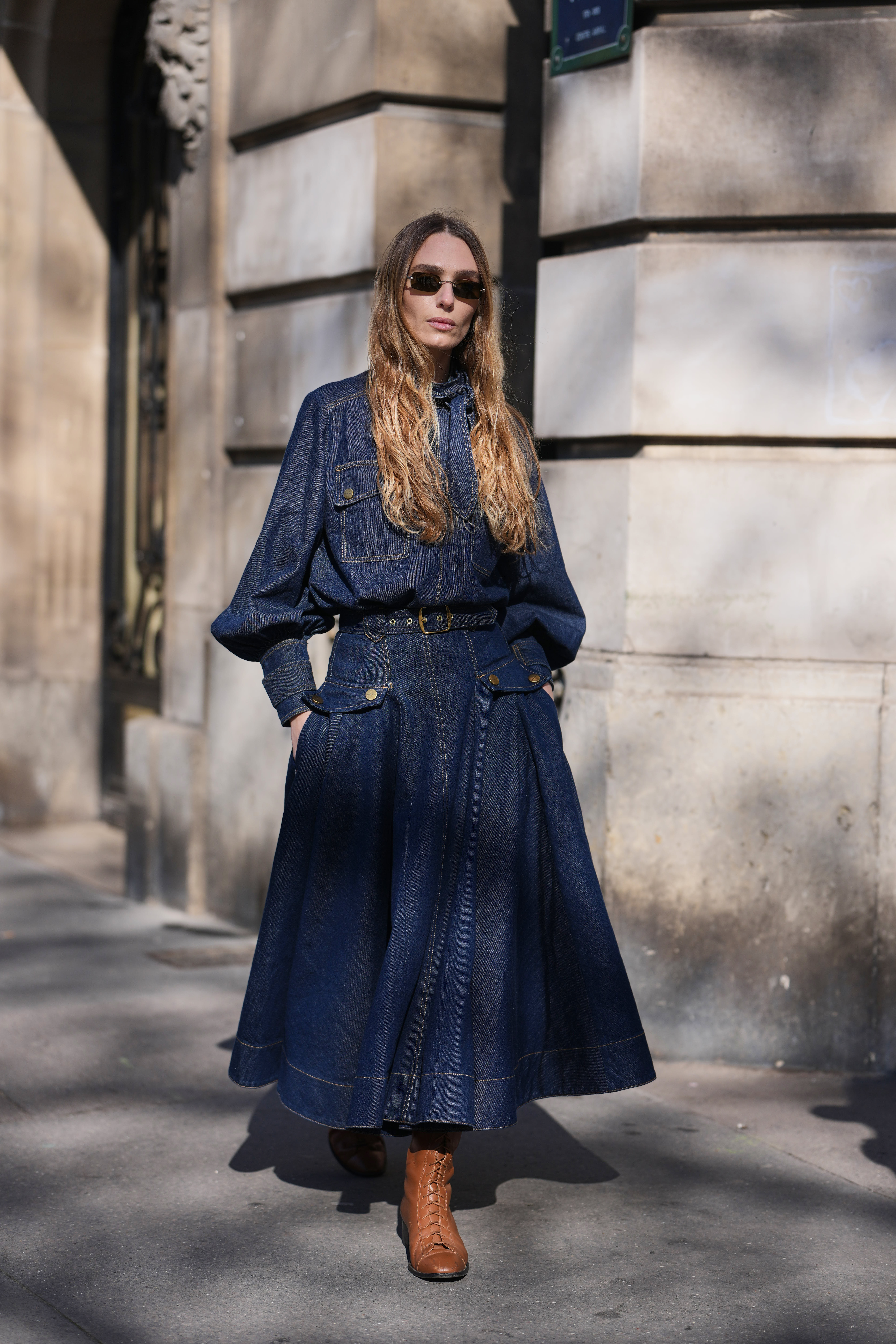 A guest wears light brown hair, dark brown sunglasses, a dark blue denim puffy sleeves / belted long sleeve maxi dress, brown leather laces ankle boots, outside Zimmermann