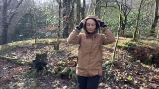 A hiker in the woods putting her hood up