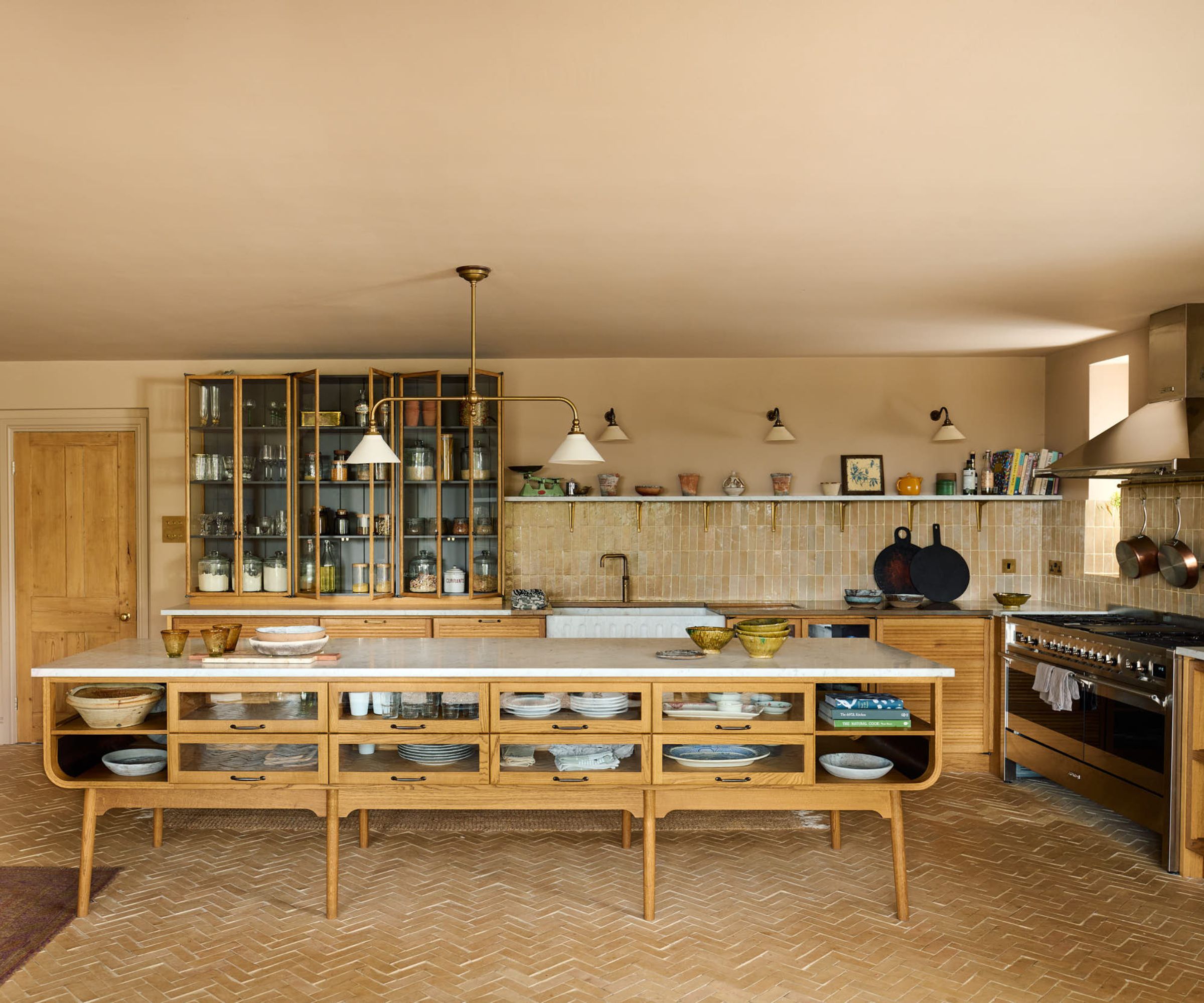 A wooden kitchen with a tile backsplash, vintage rugs, and glass-fronted cabinets