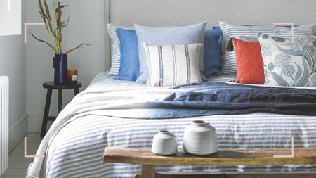 Pale grey bedroom close up of a well-made bed with blue stripe bedding and blue and coral cushions 