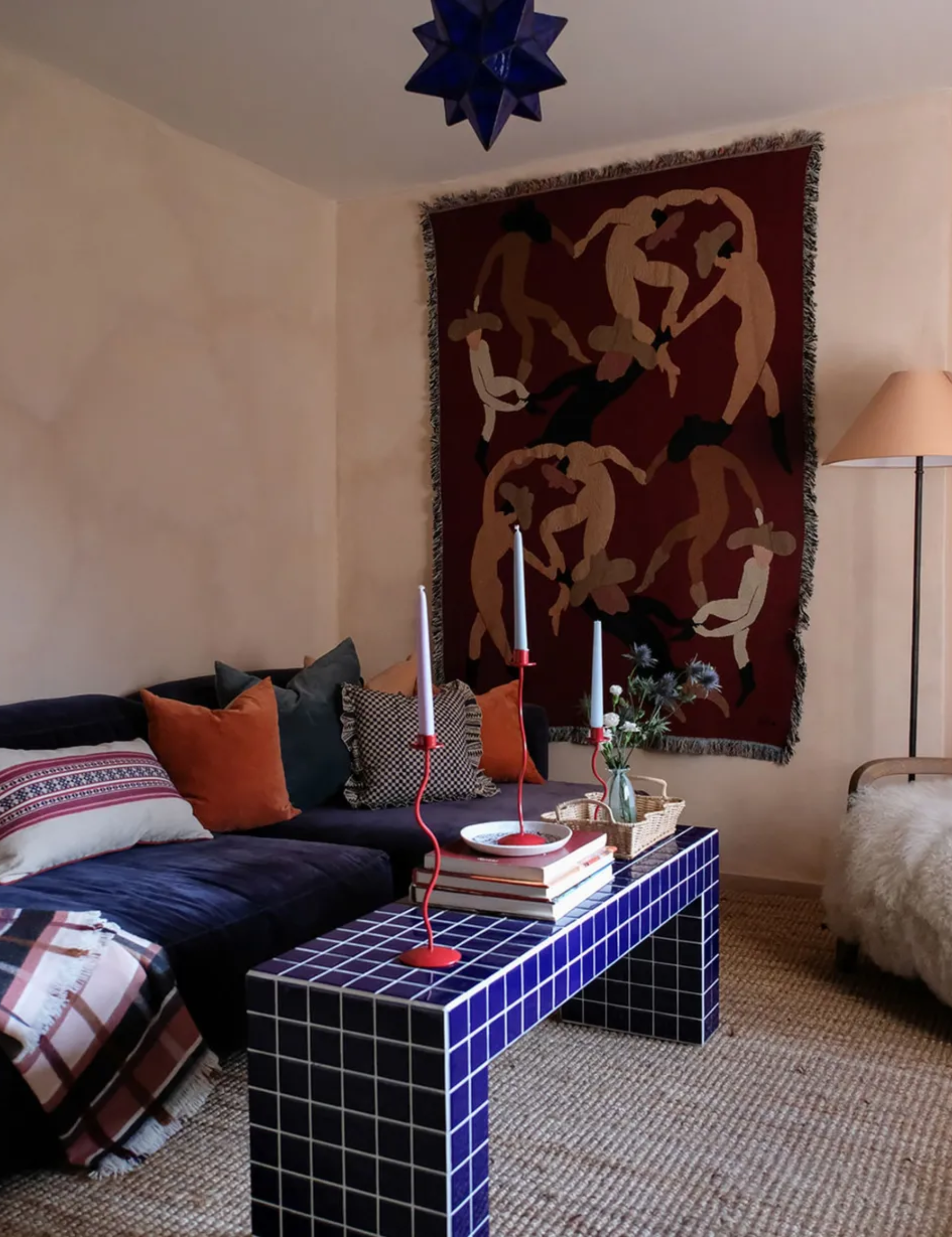 Eclectic living room with pink lime wash walls, tapestry on the wall, blue tiled coffee table, velvet sofa and colorful cushions