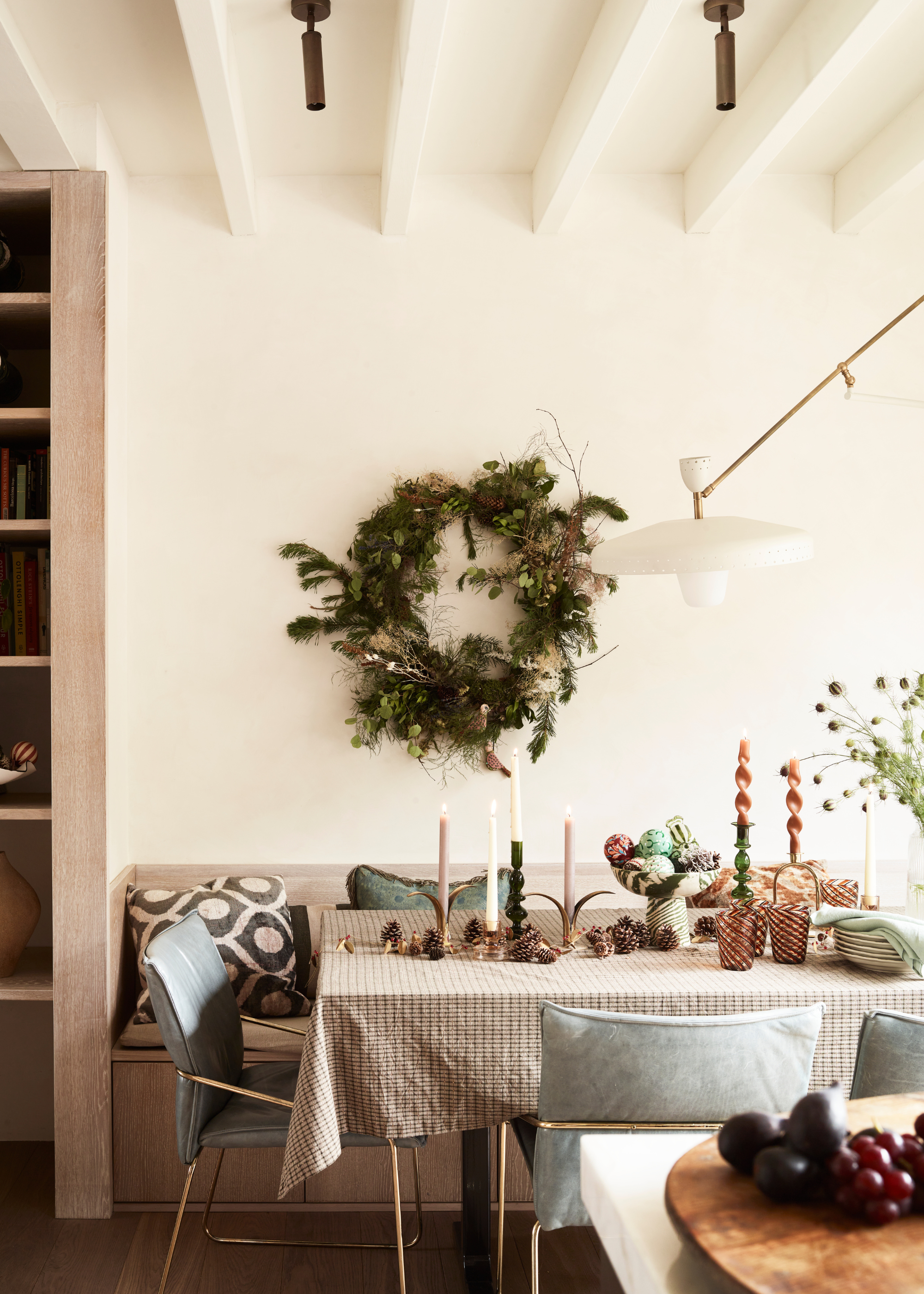 A Christmas table decorated with acorns, taper candles and a marble decorative bowl filled with baubles with a large wreath hanging in the center of the wall behind