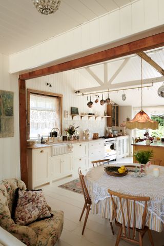 rustic kitchen/diner with white painted floorboards, white kitchen units, beams, shiplap, floral prints