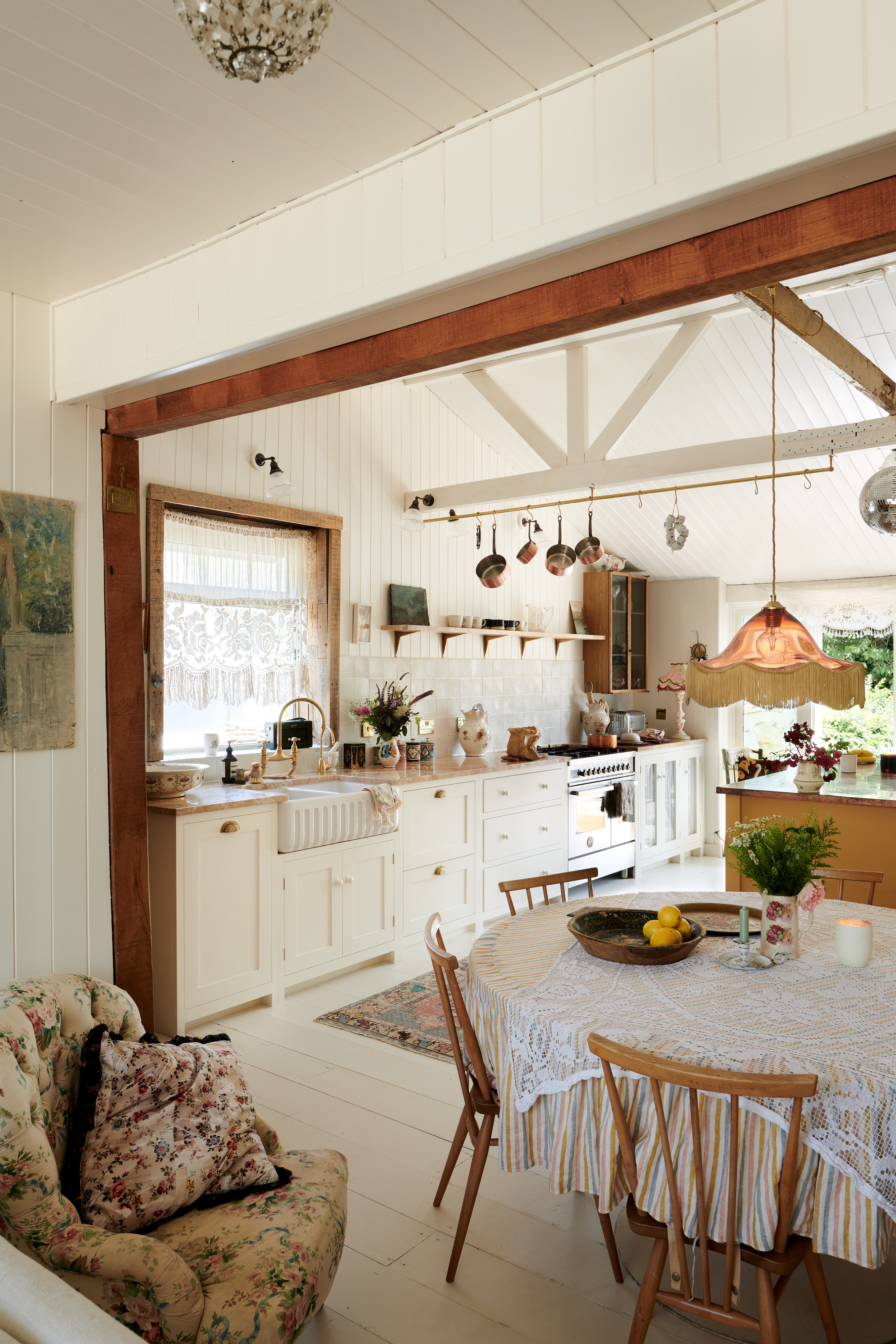 rustic kitchen/diner with white painted floorboards, white kitchen units, beams, shiplap, floral prints