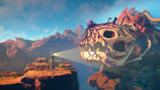 A screenshot of Double Fine's Keeper. A lighthouse stands on the edge of an arid cliff, shining its light roward a massive monster skull covered in pink vines.