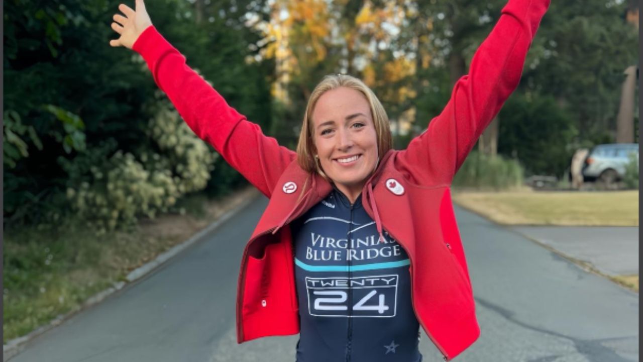 Caileigh Filmer throws her hands skyward while wearing her red Team Canada jacket and her Team Twenty24 cycling jersey.