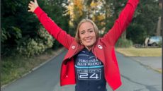 Caileigh Filmer throws her hands skyward while wearing her red Team Canada jacket and her Team Twenty24 cycling jersey.