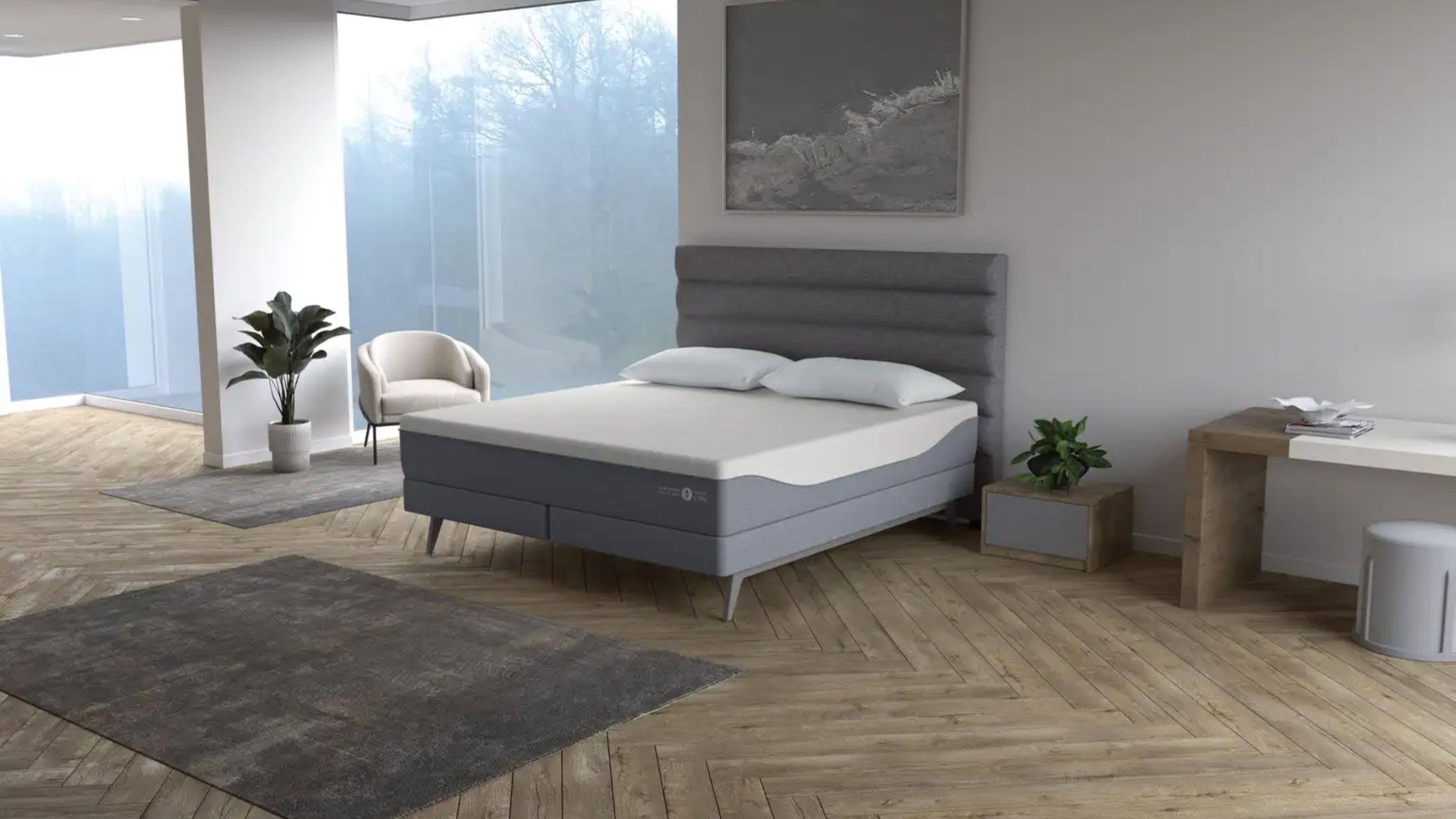 Sleep Number ClimateCool mattress in a white bedroom on a grey bedframe, with light wood parquet flooring, a desk with grey stool, white boucle chair, houseplant, and large windows