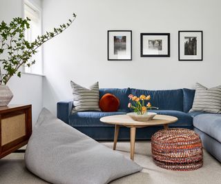 family living room with white walls and blue sectional, gray floor cushion and gallery wall