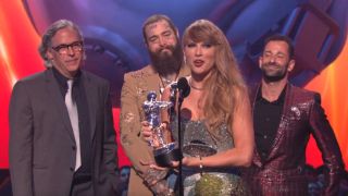 Taylor Swift giving a speech at the VMAs, with Rodrigo Prieto, Post Malone and Ethan Tobman are standing behind her.