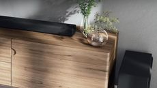 Yamaha True X Bar 50A soundbar on wooden TV cabinet with two small plant vases, next to subwoofer.