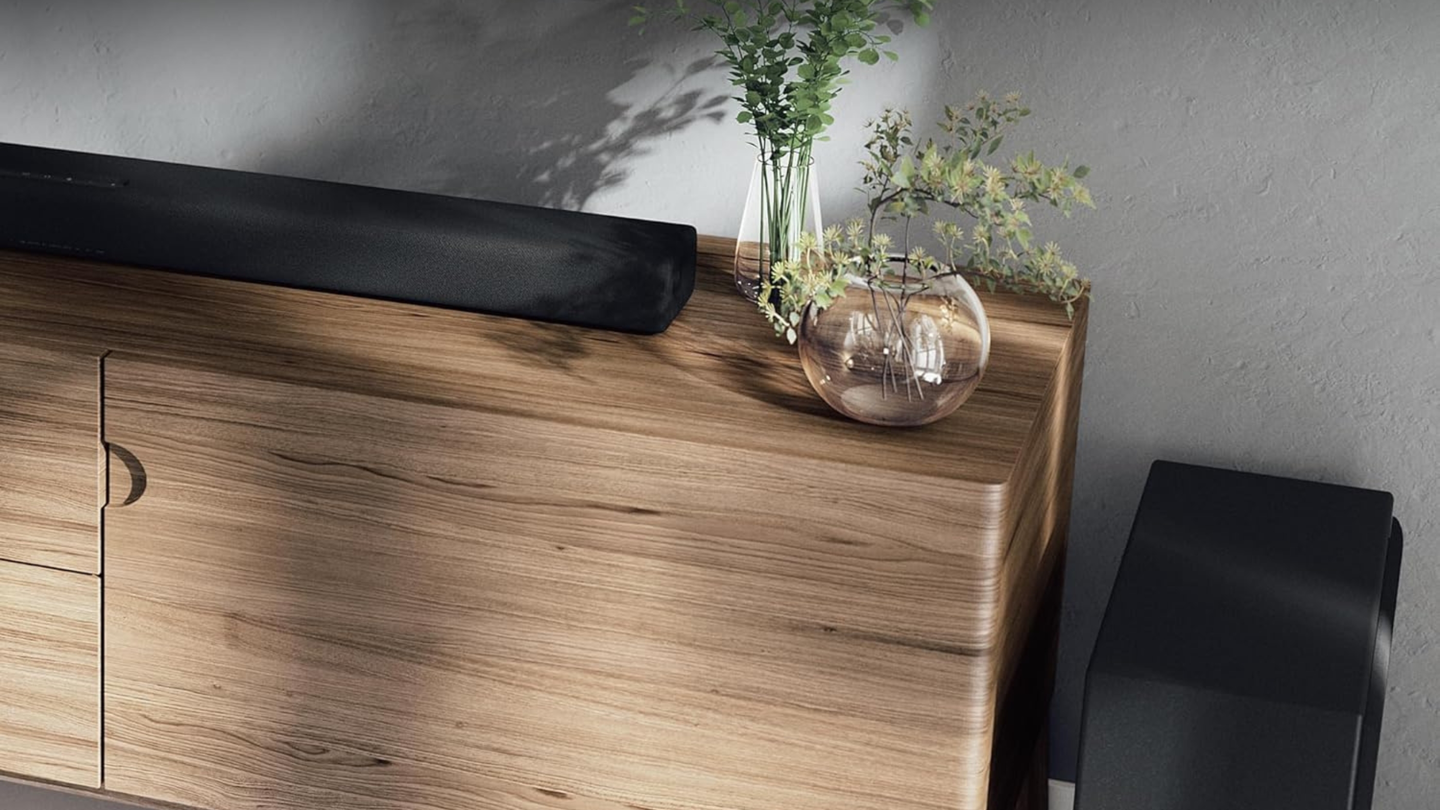 Yamaha True X Bar 50A soundbar on wooden TV cabinet with two small plant vases, next to subwoofer.