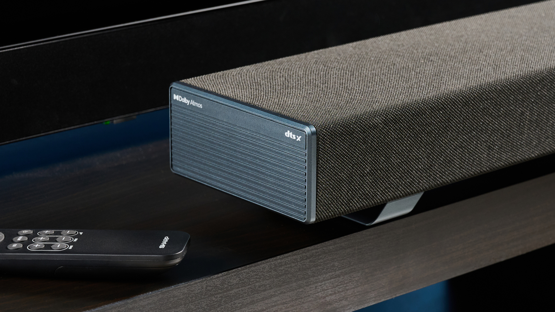 the Sharp 3.1.2 HT-SBW53121 Soundbar in black with a remote, subwoofer, against a blue background next to a panasonic TV