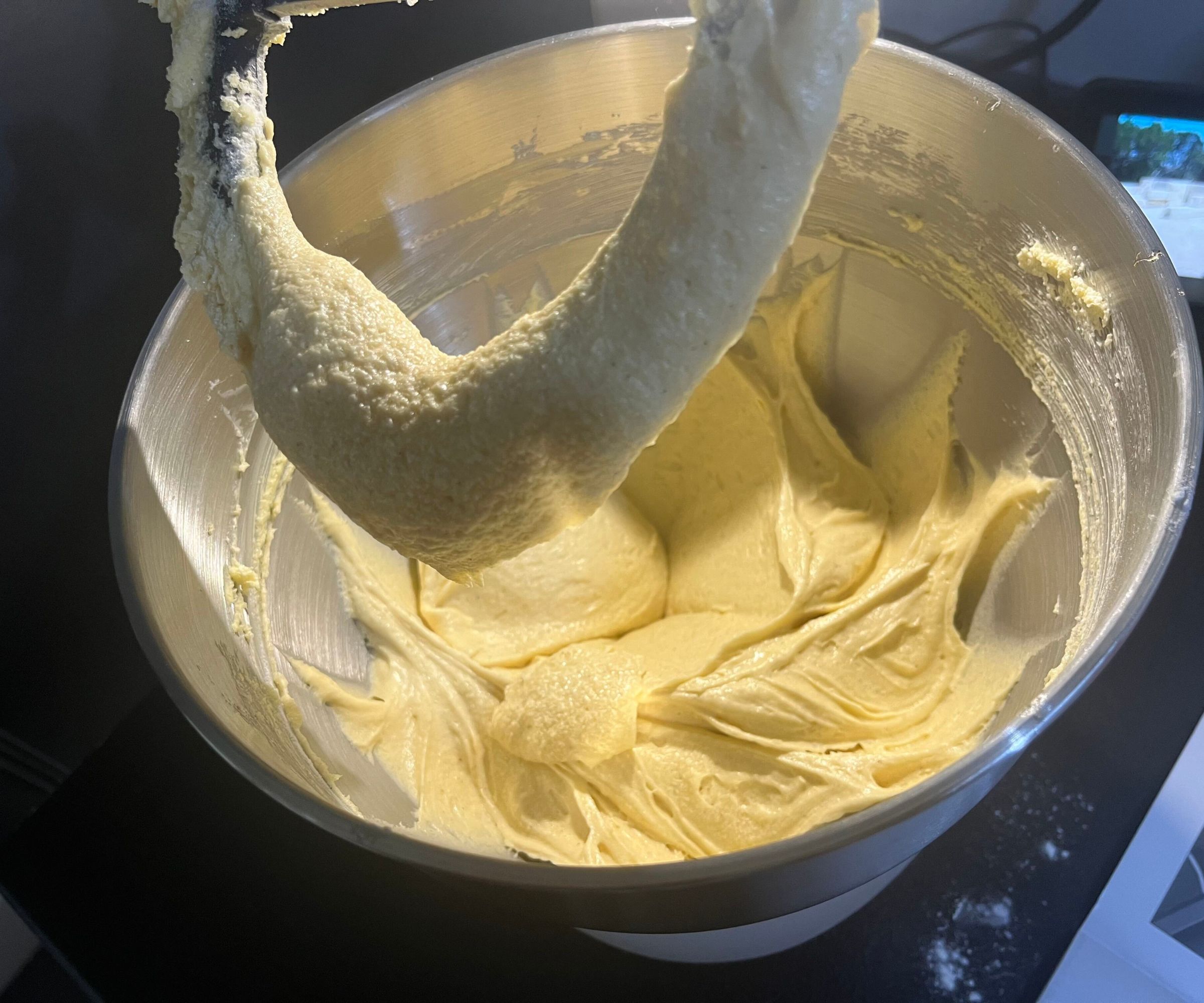 Light colored cake batter inside a stainless steel mixing bowl, with a overed paddle above it.