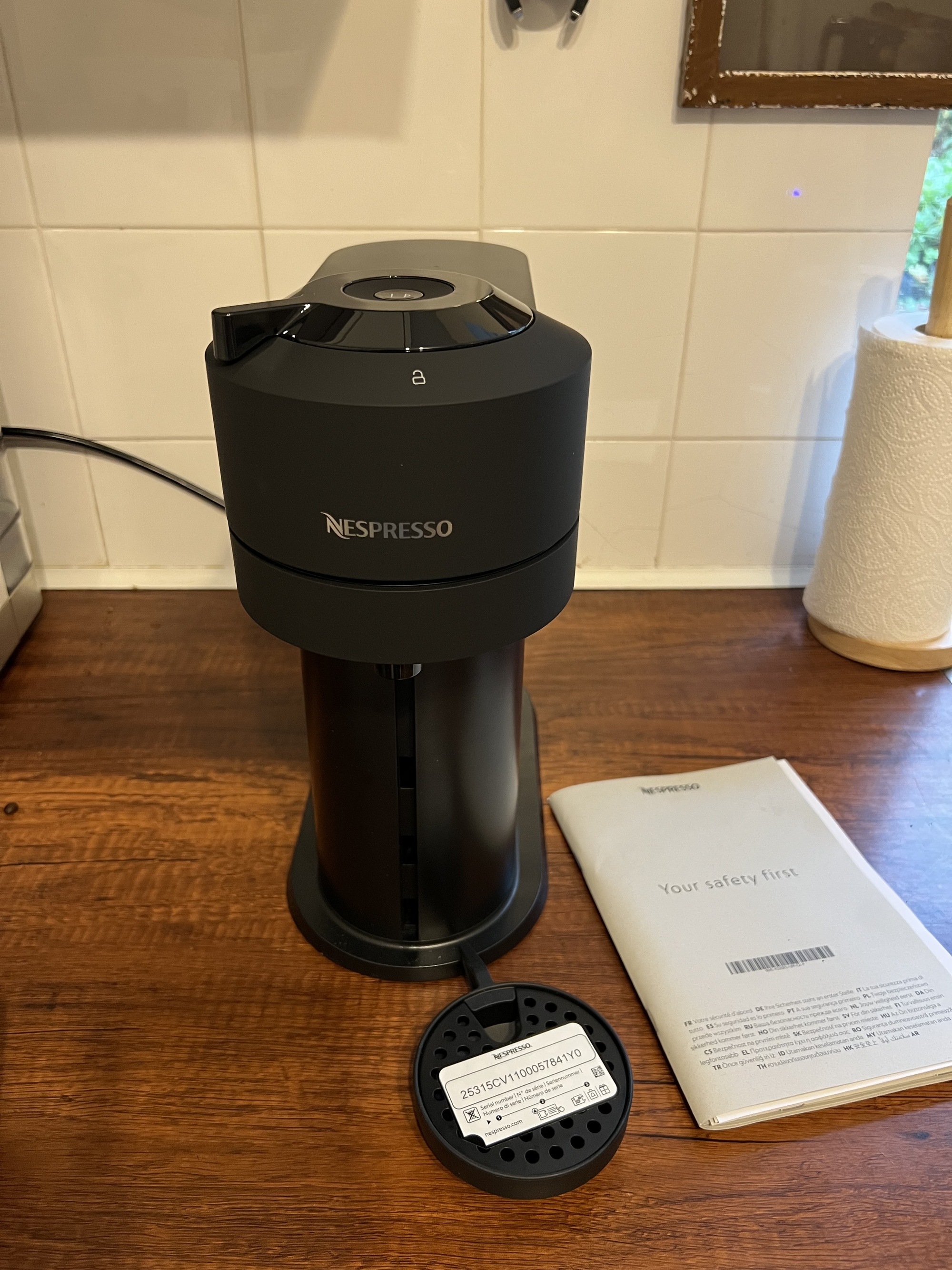 Black Nespresso Vertuo Next machine on a wooden countertop with a safety manual next to it.