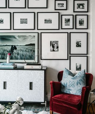 A living room with a black and white gallery wall and a red armchair