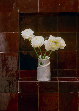 A small white vase of flowers on a nook decorated with burgundy tiles